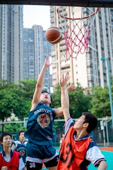 Teens playing a competitive street basketball game amidst urban skyscrapers.
