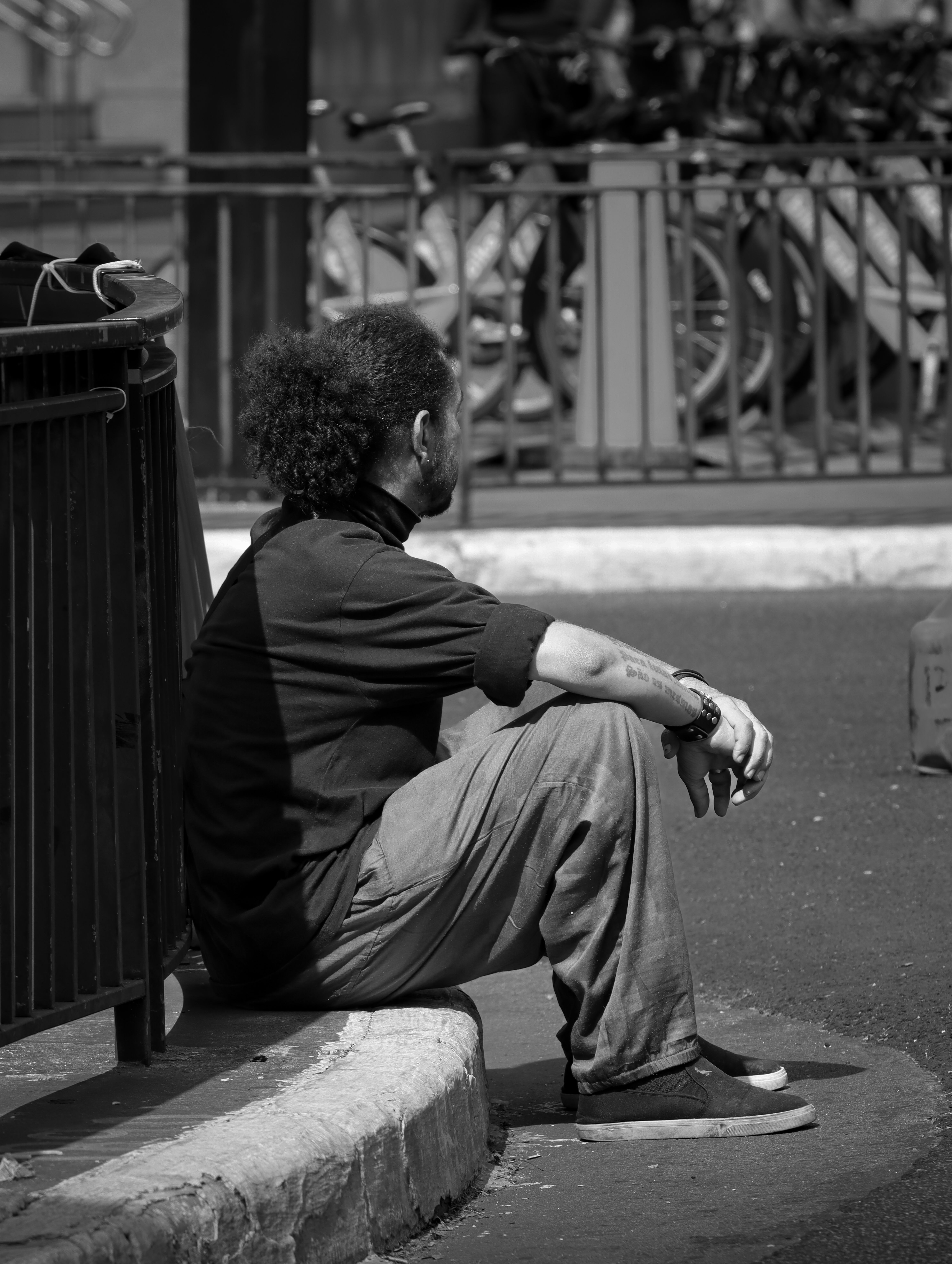 Black and white photo of a man sitting thoughtfully on a city street curb, capturing urban life.