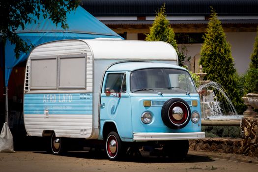 Charming vintage blue food truck with attached trailer parked outdoors near a fountain.