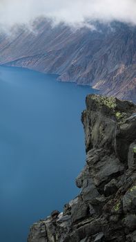 Breathtaking view of Changbai Mountain's crater lake and rocky cliff under misty sky.