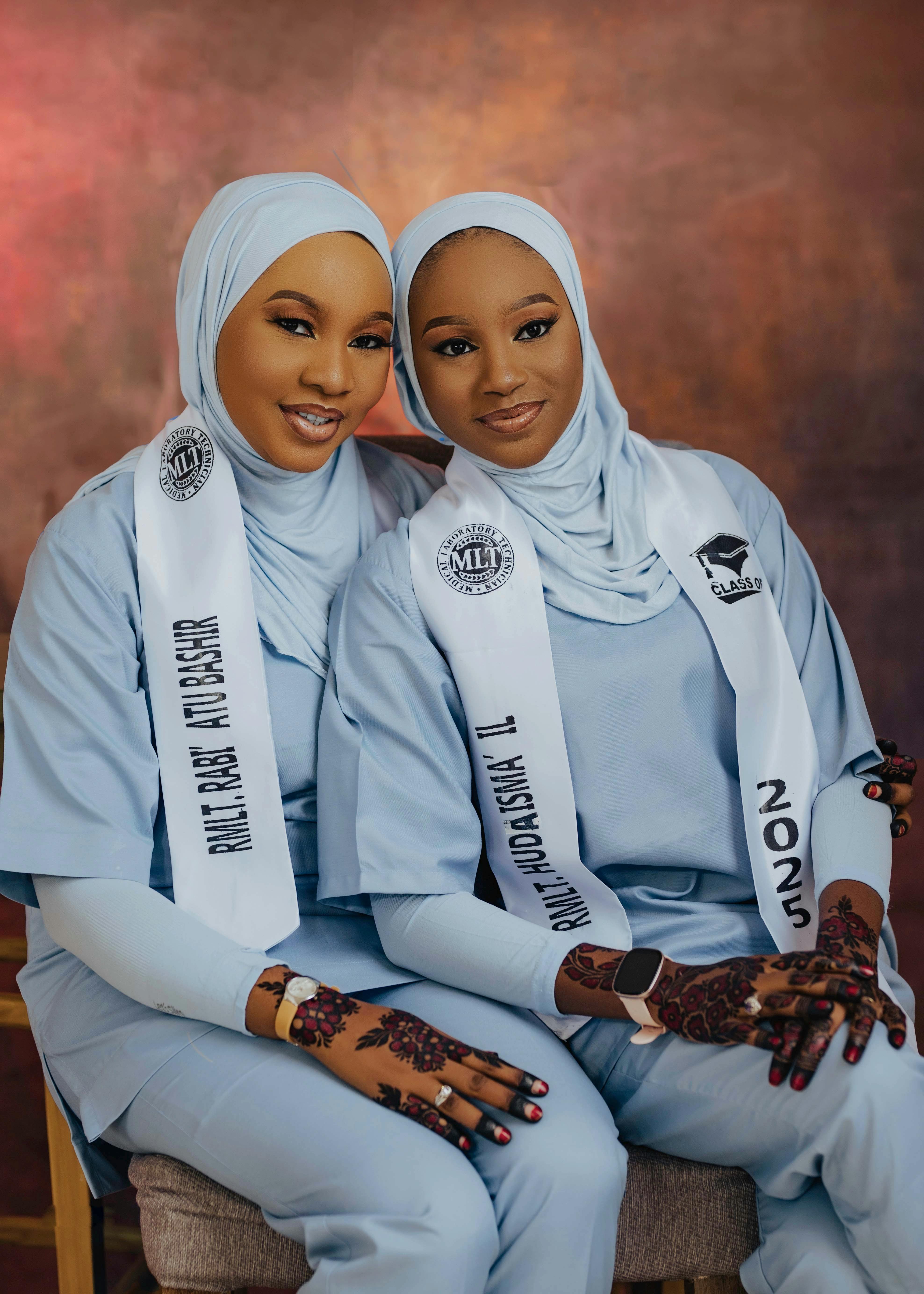 Two female graduates in matching attire proudly display their achievements.