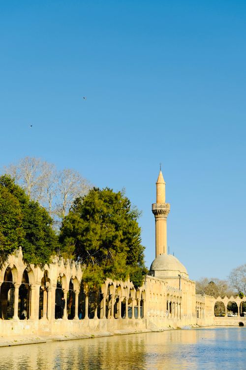 Free Beautiful ancient mosque with minaret by water and trees under a clear blue sky. Stock Photo