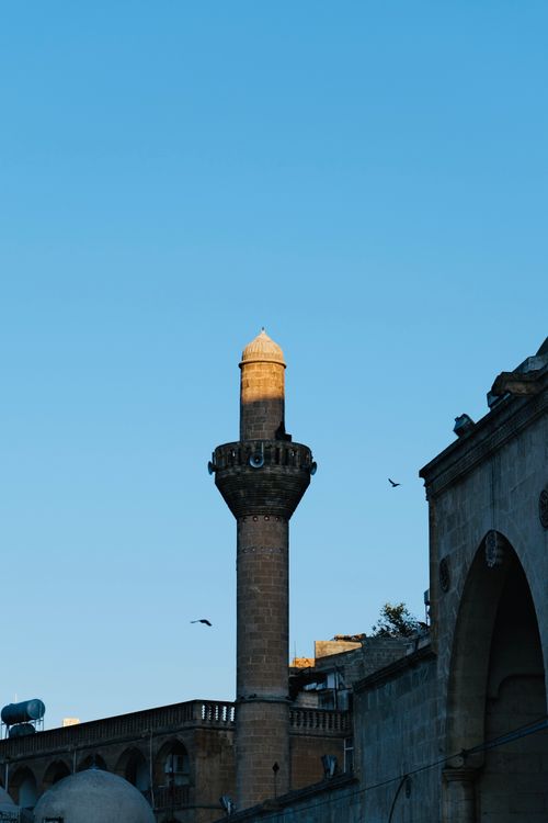 Free A beautiful minaret silhouetted against a clear blue sky with birds flying nearby. Stock Photo