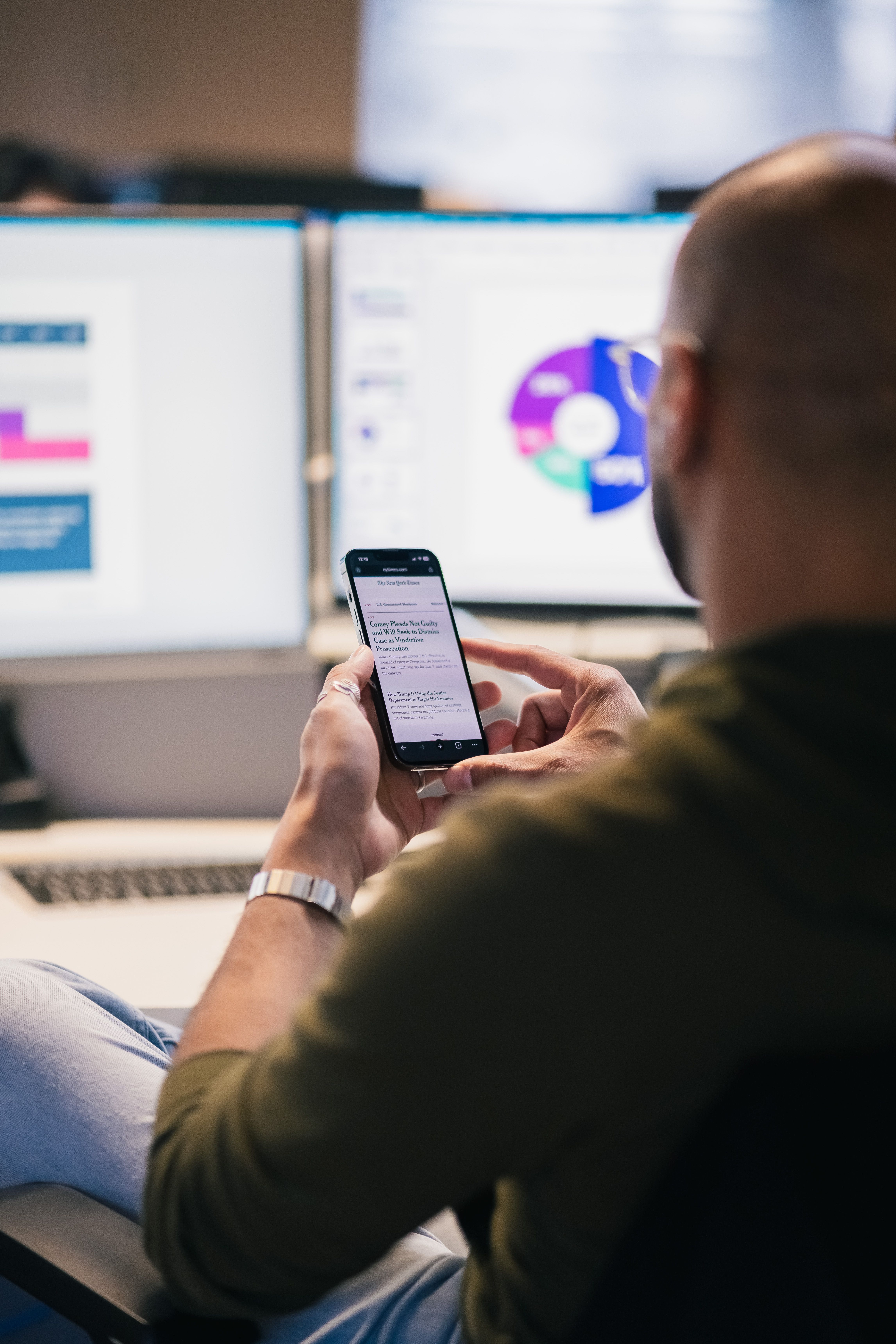 Profissional acompanhando dados de negócios em múltiplas telas enquanto utiliza o smartphone