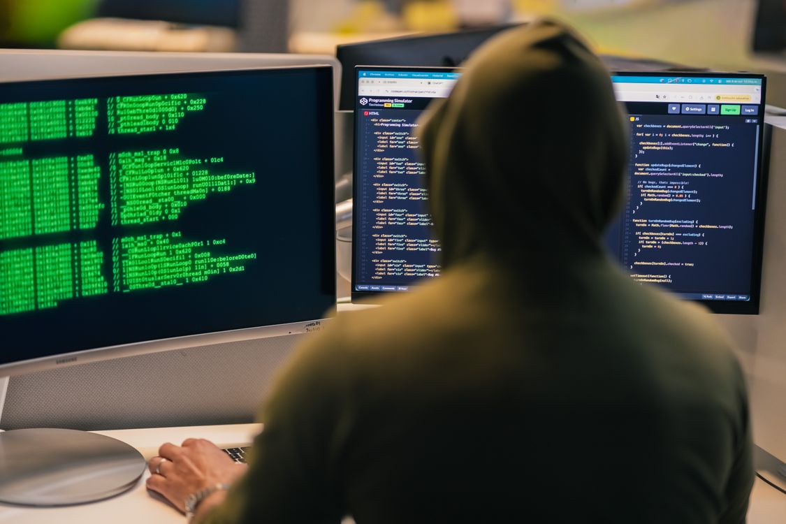 Programer u kapuljači kodira na dva monitora u mračnoj prostoriji