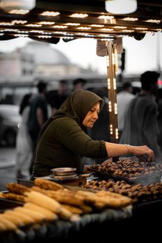 A woman vendor selling roasted chestnuts at a street stall in Istanbul, Türkiye, at twilight.