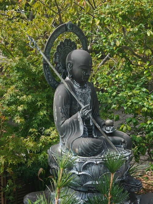 Free A tranquil stone statue surrounded by lush green leaves and plants, depicting calmness and peace. Stock Photo