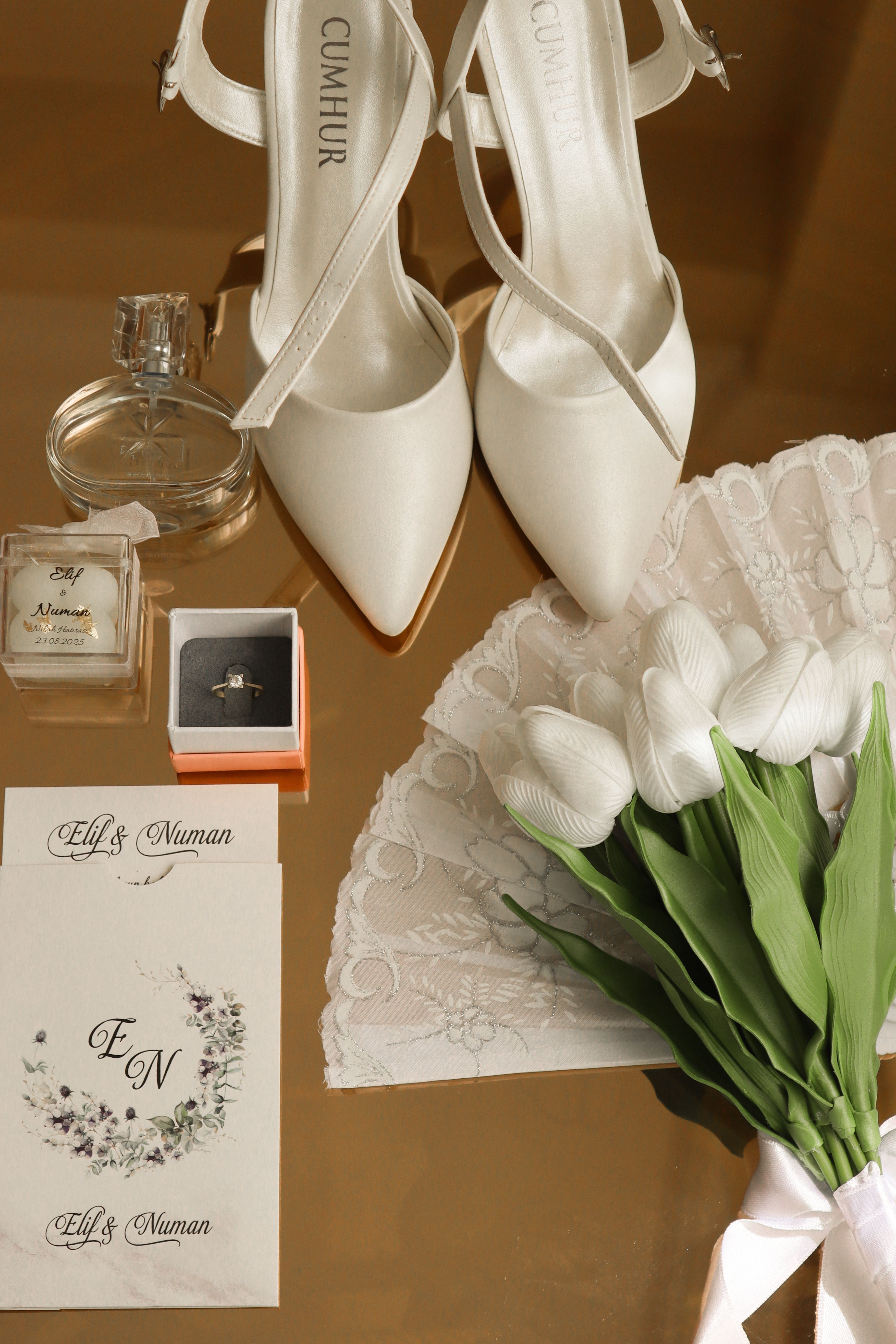 Flat lay of wedding items including white shoes, bouquet, invitations, and perfume.