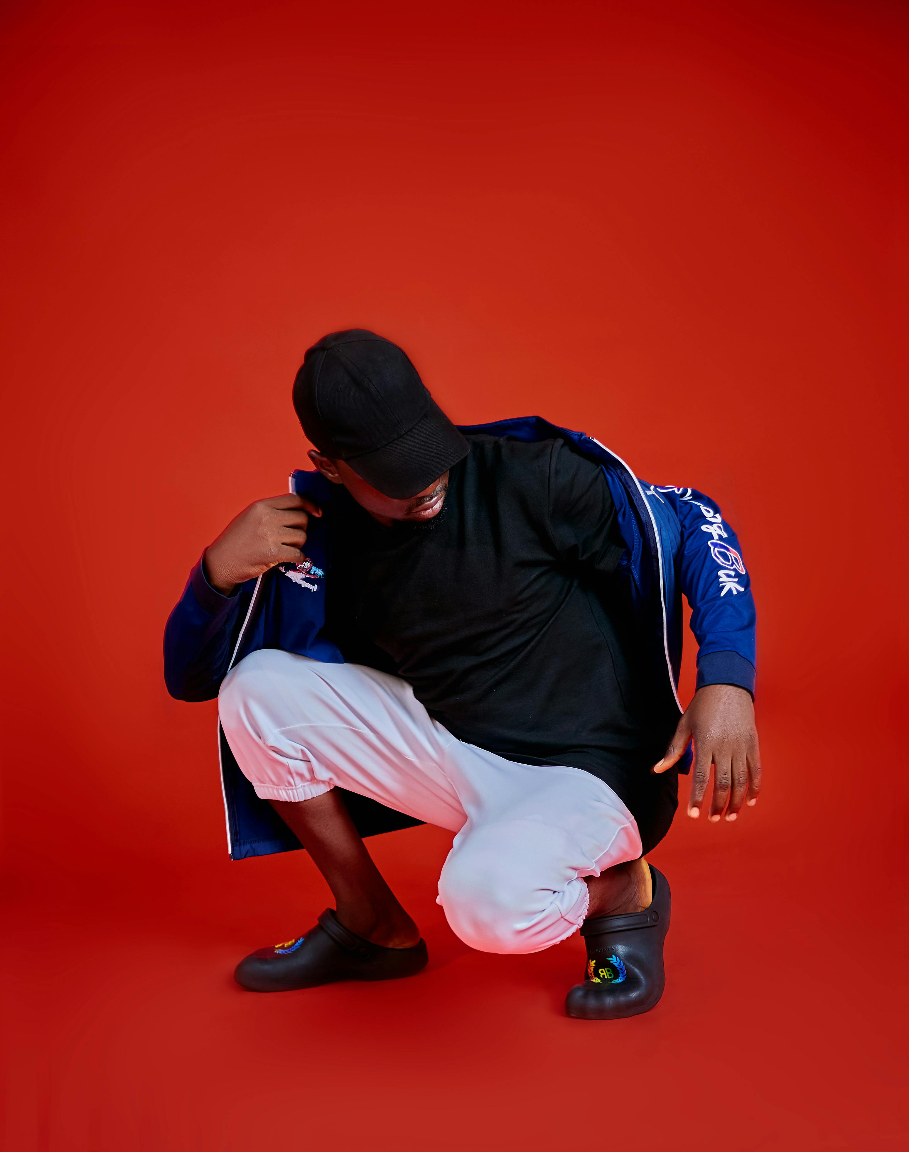 Man in casual streetwear posing dynamically on a vivid red backdrop.