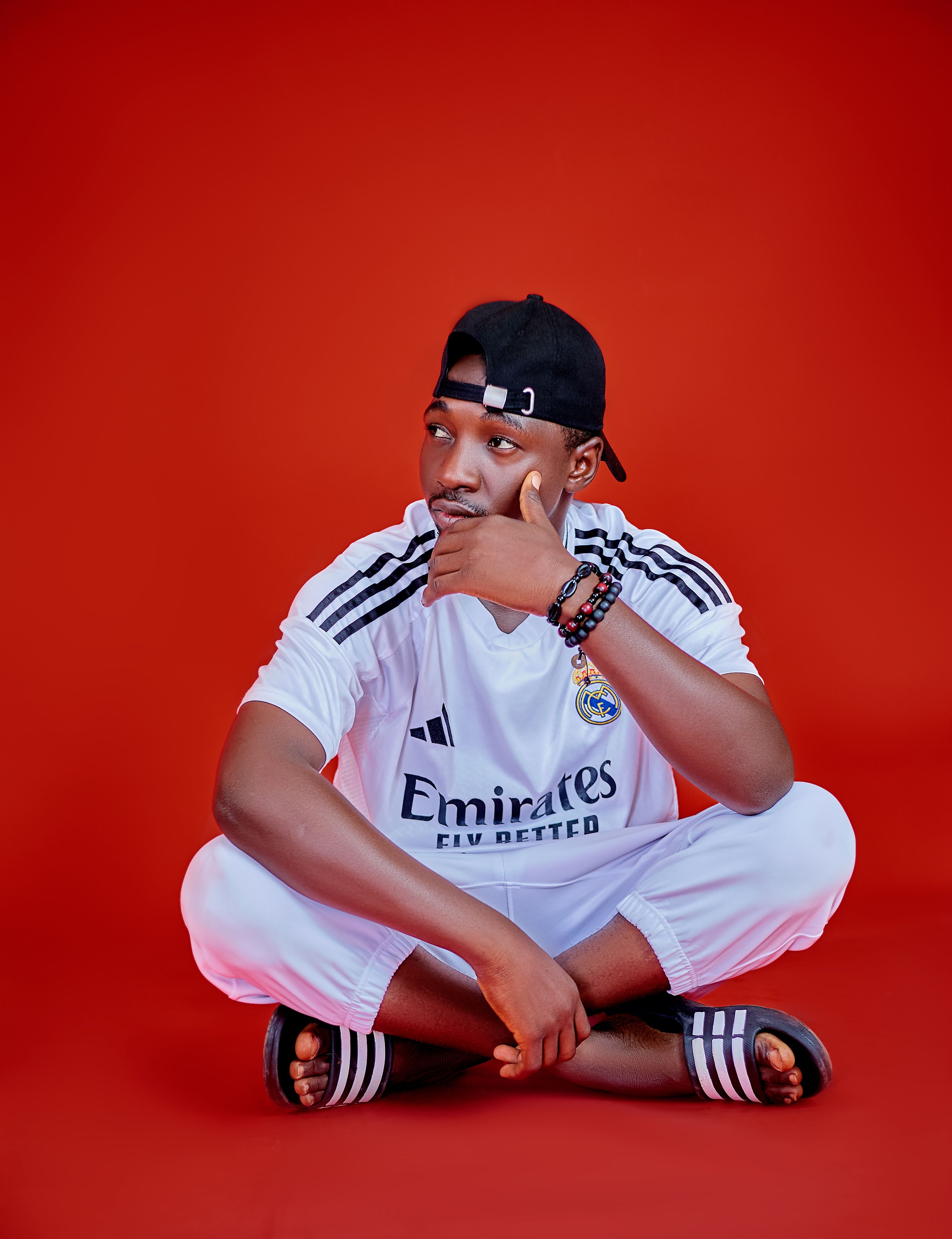 Young man sitting casually in sportswear on a vibrant red backdrop.