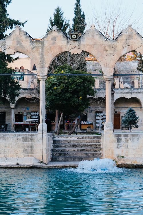 Free Tranquil scene of historic stone arches and a fountain with vibrant blue water. Stock Photo