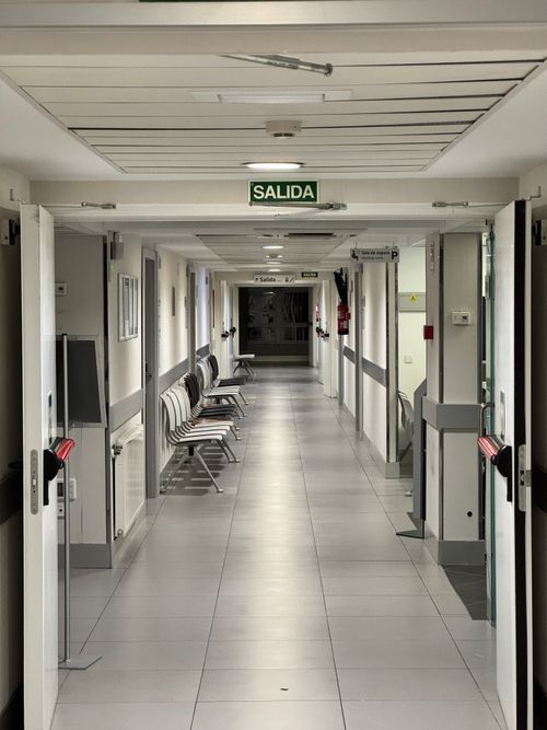 Free Long empty hospital corridor with exit sign, emphasizing cleanliness and sterility. Stock Photo