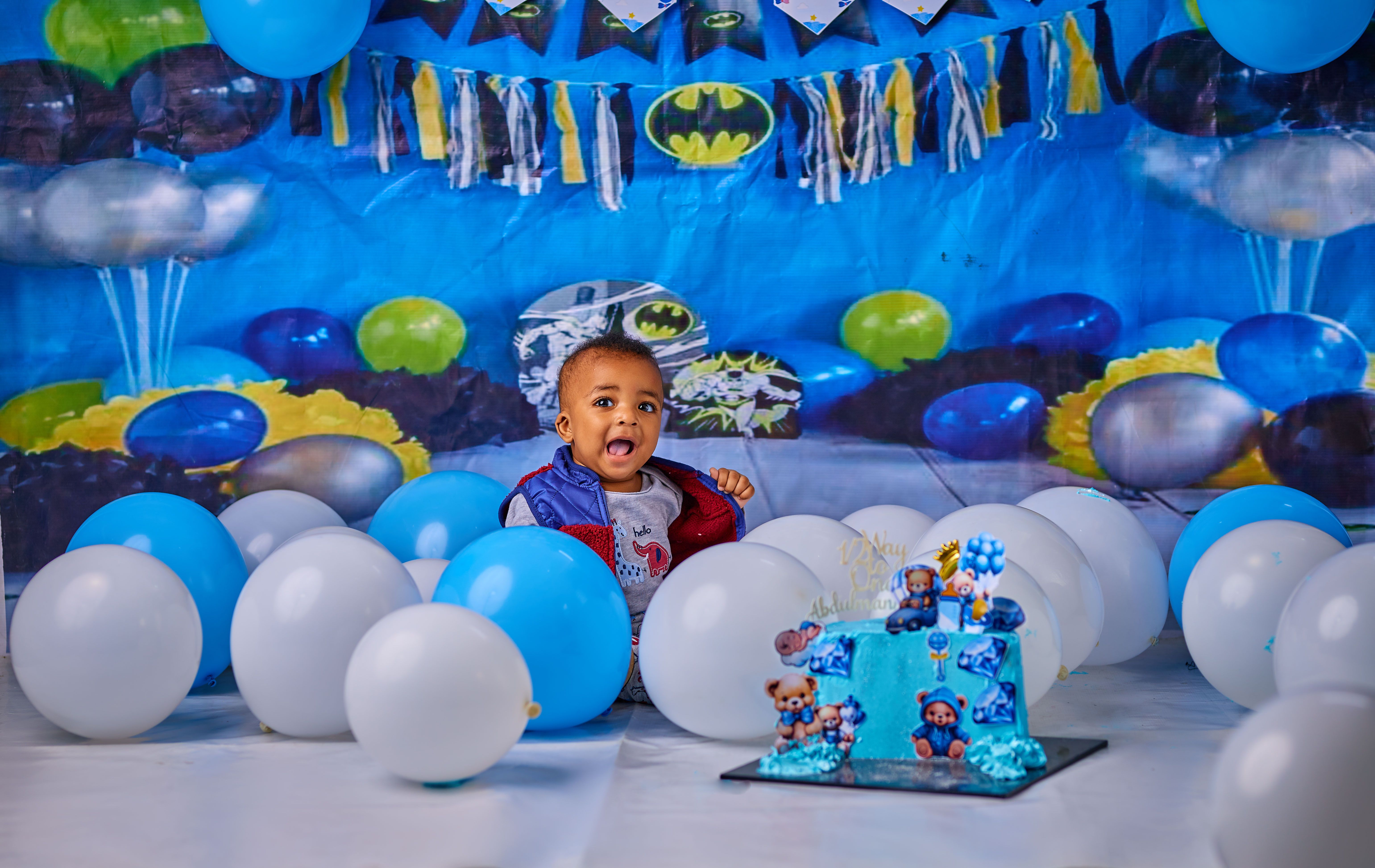 Adorable baby celebrating first birthday with balloons and cake.