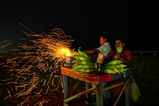 Dynamic nighttime scene of a street vendor grilling corn on Chennai beach, sparks flying.