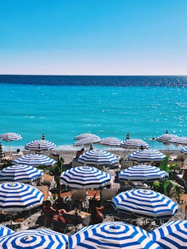 Explore the stunning azure waters and vibrant beach scene of Nice, France, featuring iconic striped umbrellas.