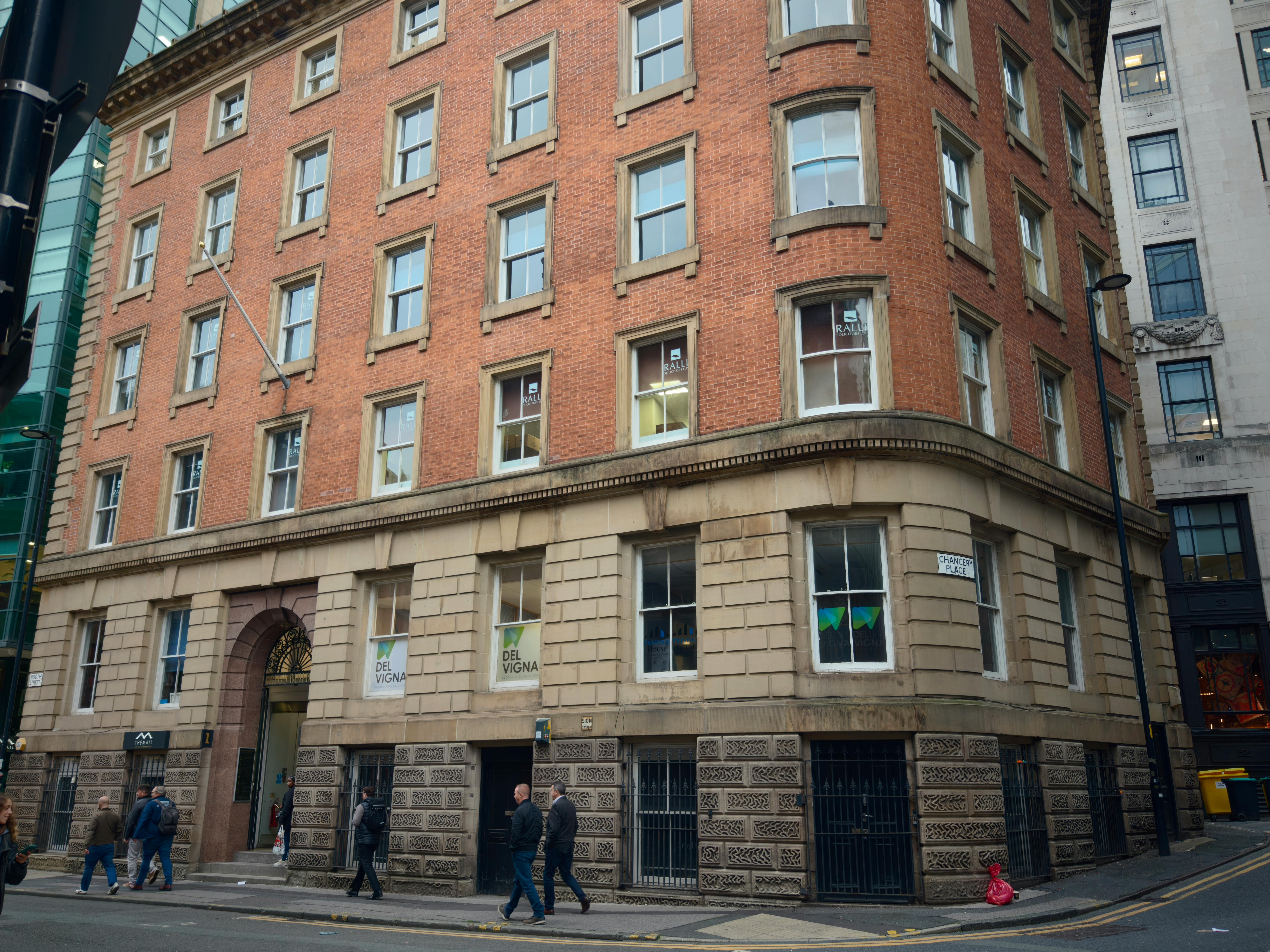 Free Red brick building on a street corner with pedestrians during the day. Stock Photo