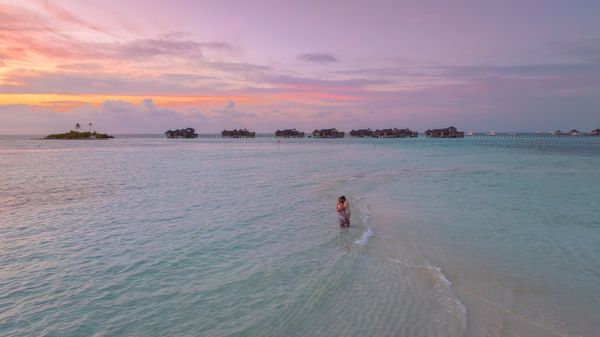 Couple embracing in shallow turquoise waters at sunset in the Maldives