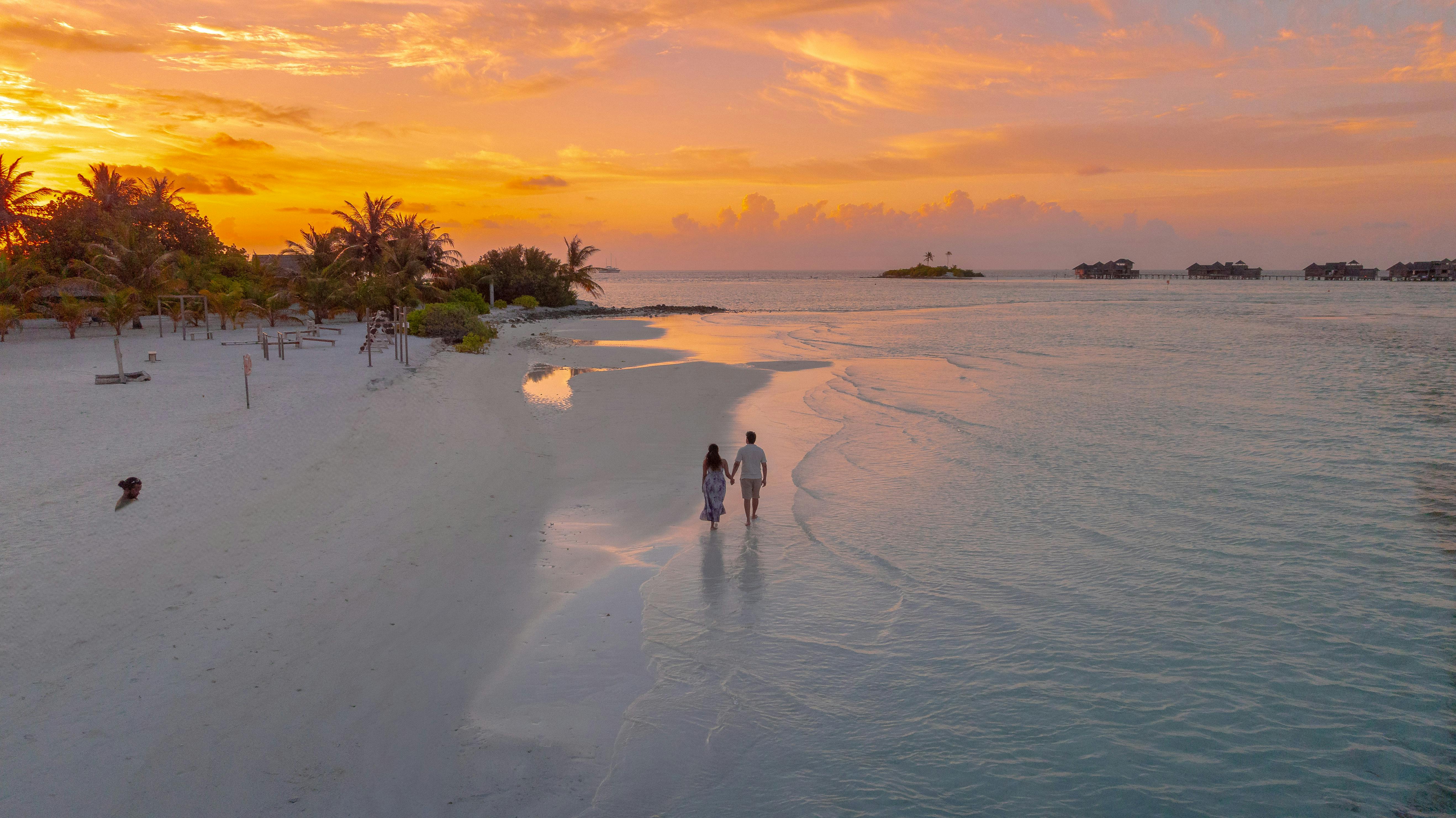 Kostenlos Ein Paar geht bei Sonnenuntergang an einem ruhigen maledivischen Strand spazieren und fängt Romantik und Ruhe ein. Stock-Foto