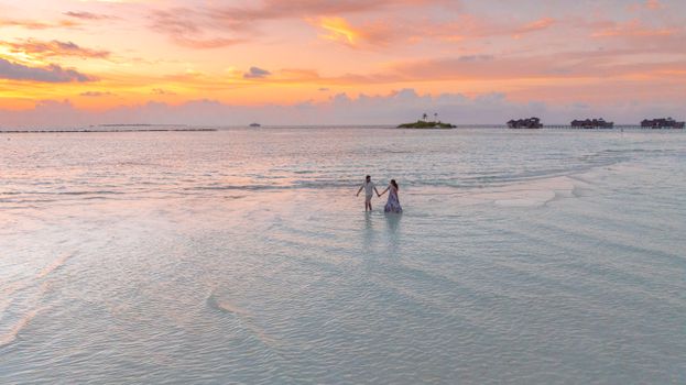 A couple walks on a serene beach in the Maldives with a stunning sunset backdrop.