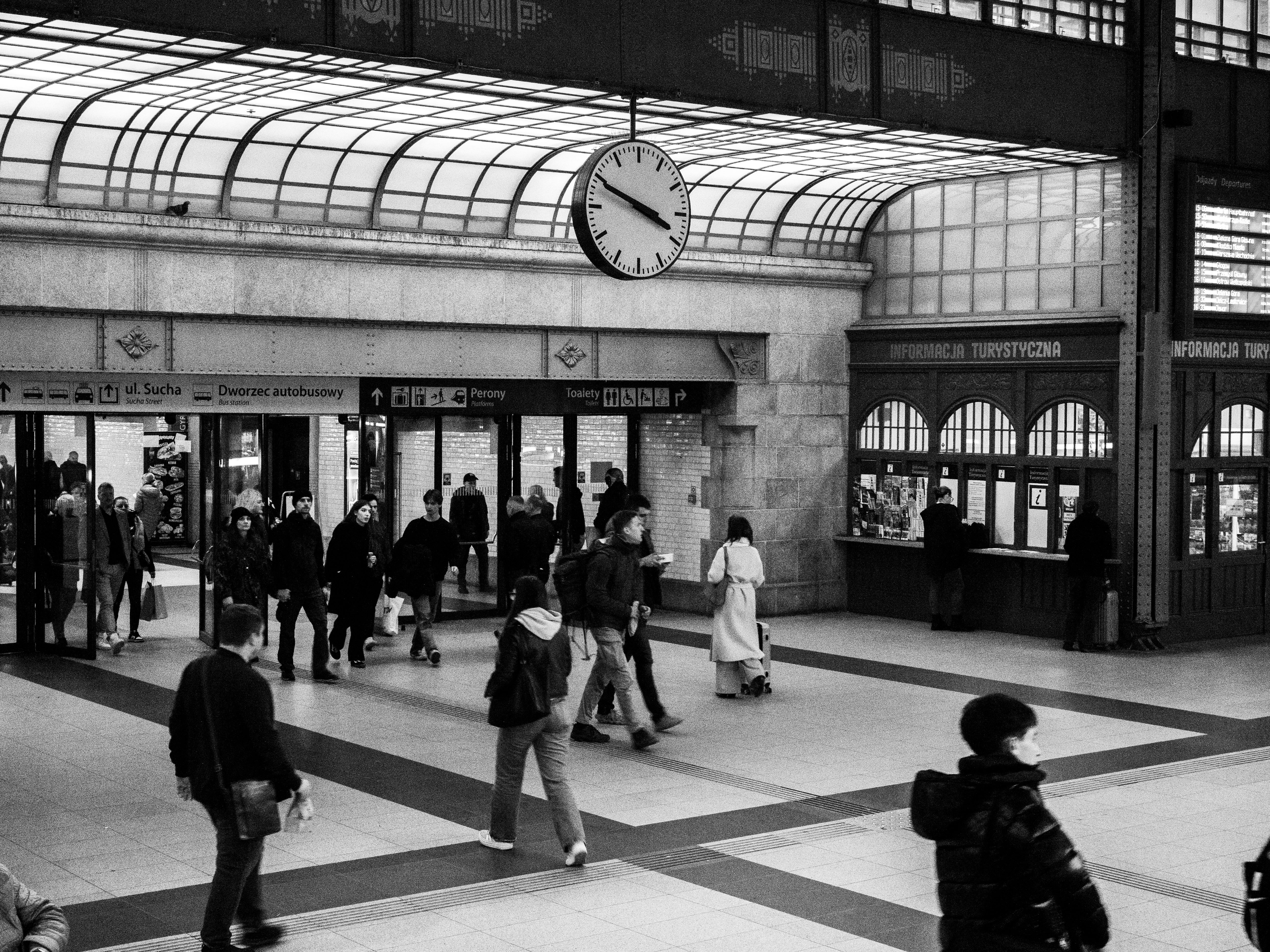 Monochrome view of a crowded train station with a prominent clock and ticket counters.