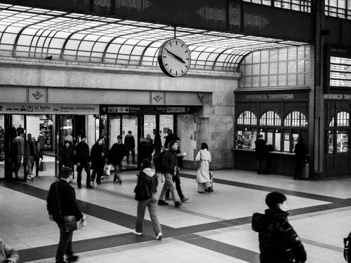 Free Monochrome view of a crowded train station with a prominent clock and ticket counters. Stock Photo