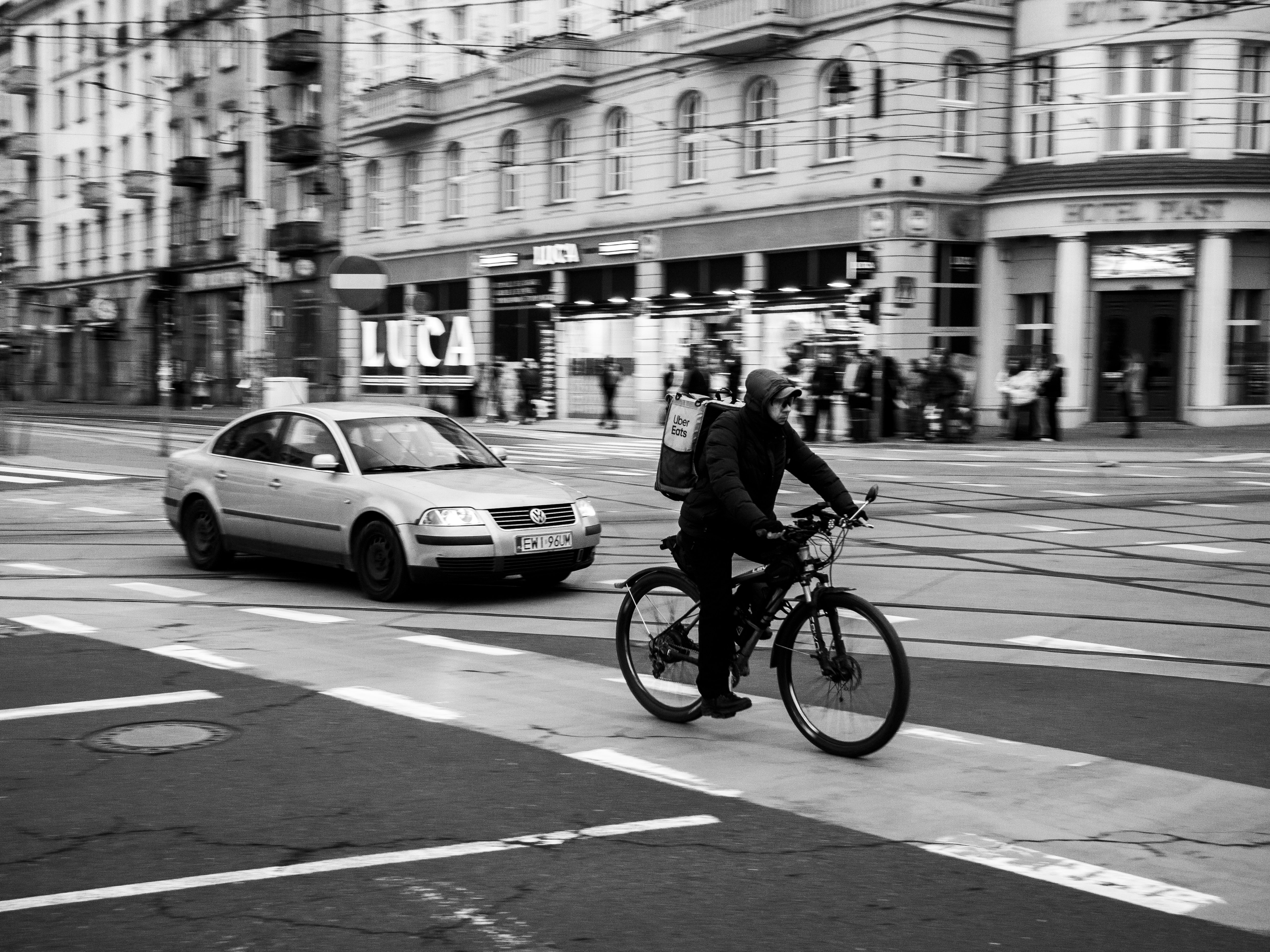 Monochrome photo of a cyclist riding on a city street with passing cars. Urban life captured in motion.