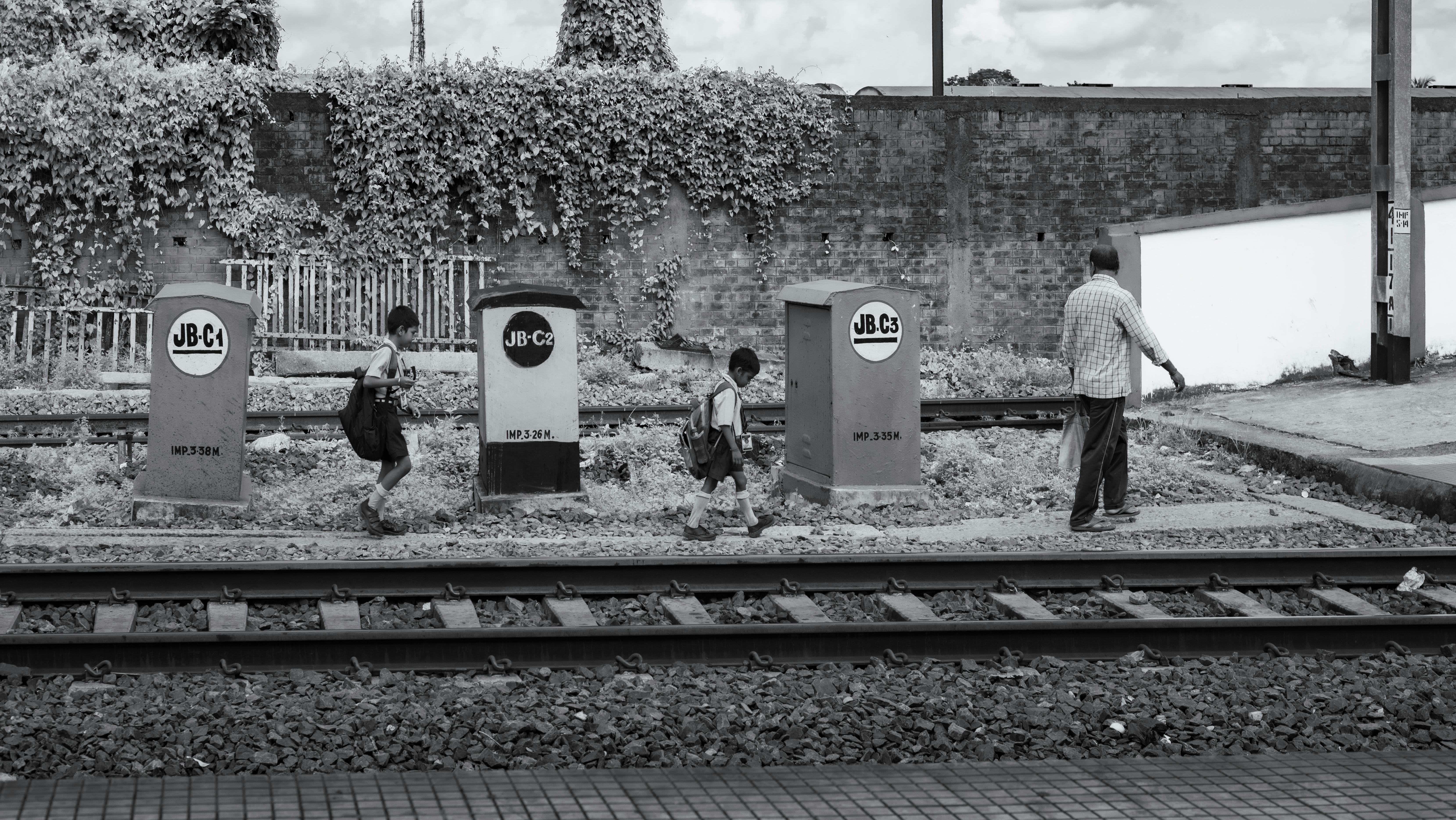 Gratuit Enfants traversant des voies ferrées sous la surveillance d'un adulte dans un décor monochrome. Photos