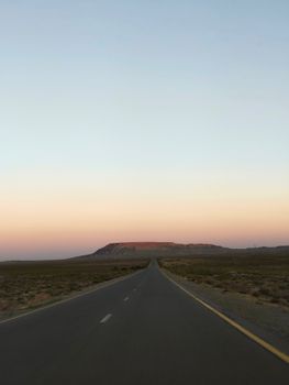 A lone desert highway stretches towards a dusky horizon under a pastel twilight sky.