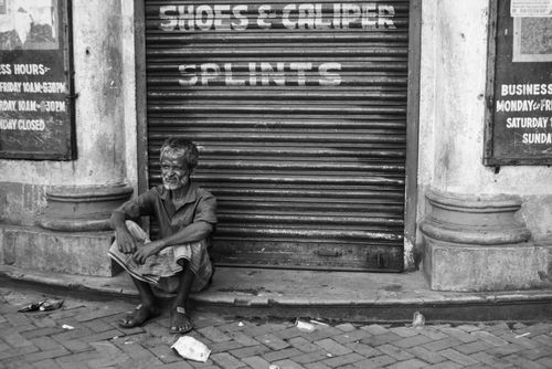 Free Reflective street portrait of a man sitting outside a closed shop. Stock Photo