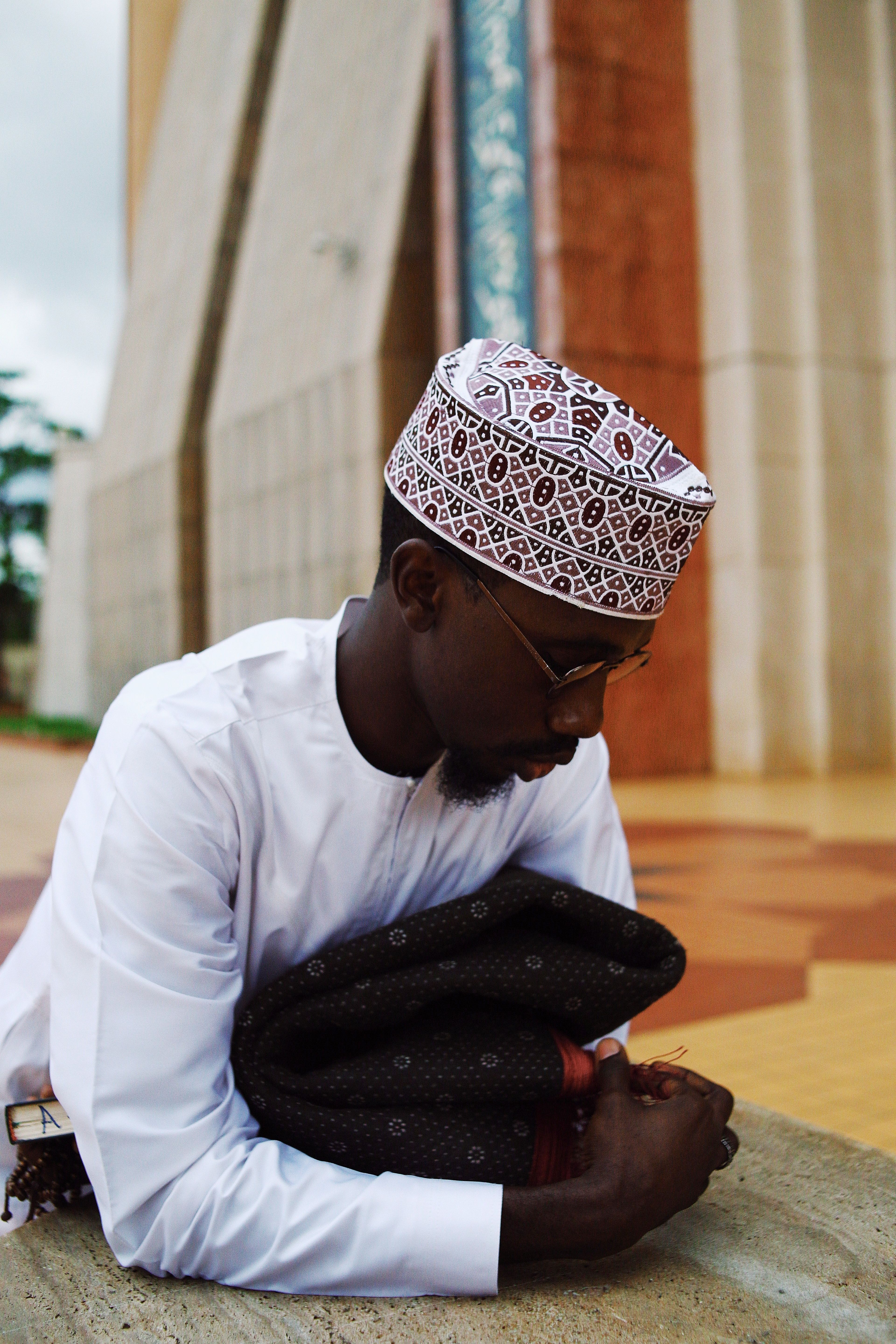 African man dressed traditionally, praying outside a landmark building in Abuja, Nigeria.
