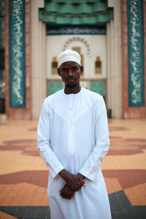 Free A man in traditional white attire standing in front of architectural details in Abuja, Nigeria. Stock Photo