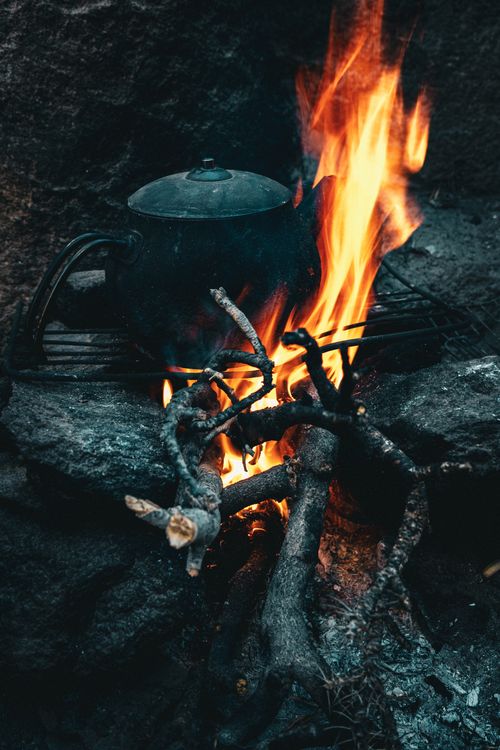 Free A pot heats over a campfire, surrounded by stones and logs, in an outdoor setting. Stock Photo