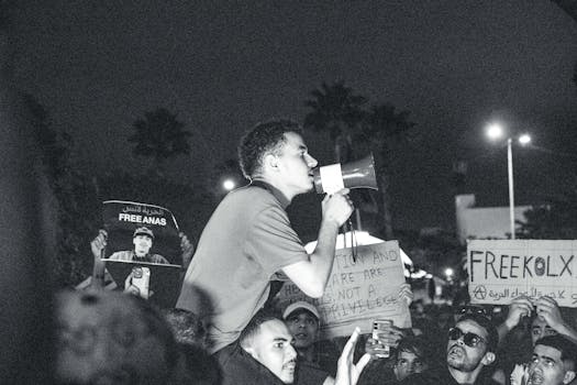 Black and white image of a protest with a young man speaking into a megaphone at night.