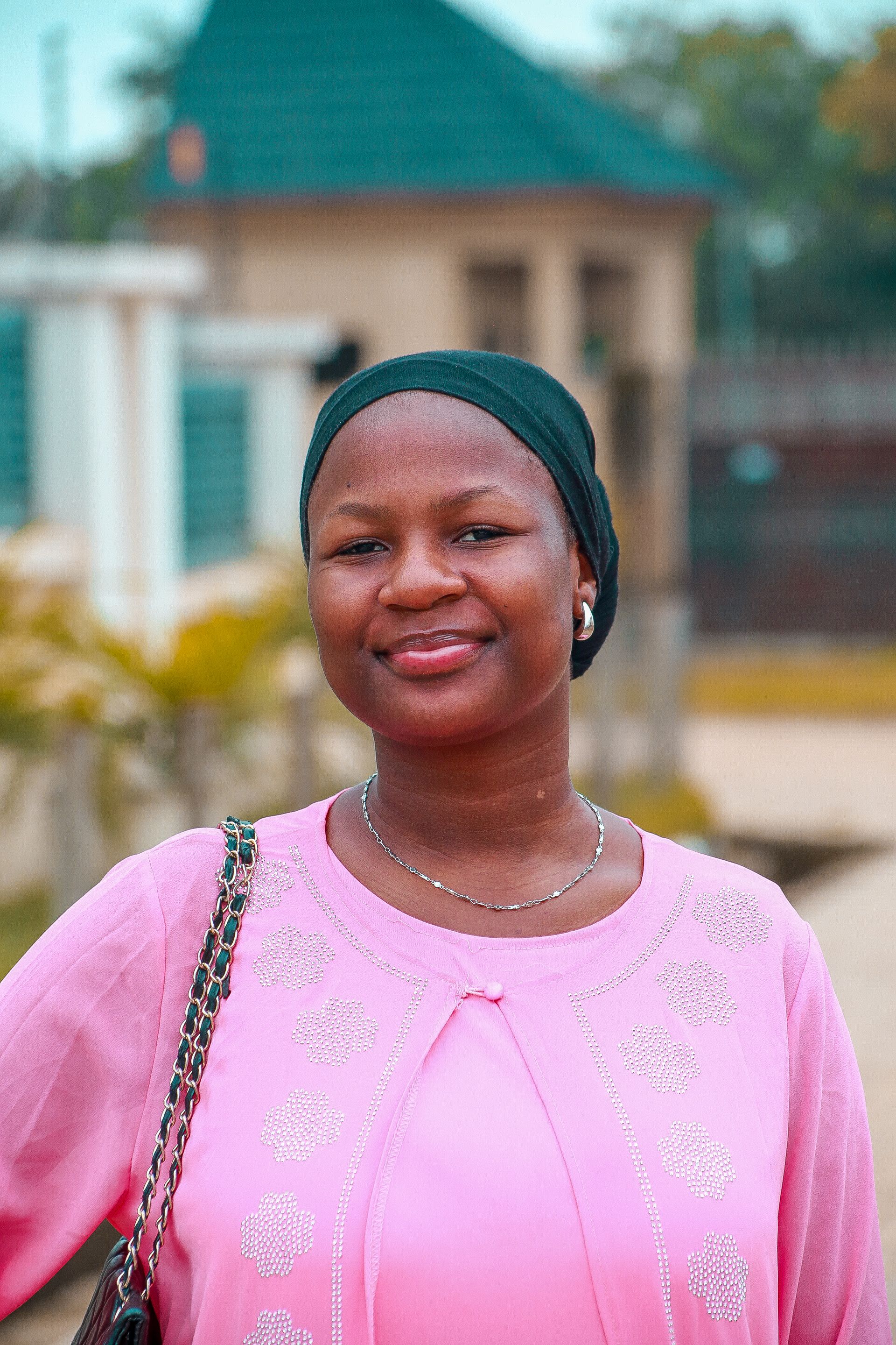 A cheerful woman wearing a pink top and headscarf smiles outdoors. Perfect for lifestyle themes.