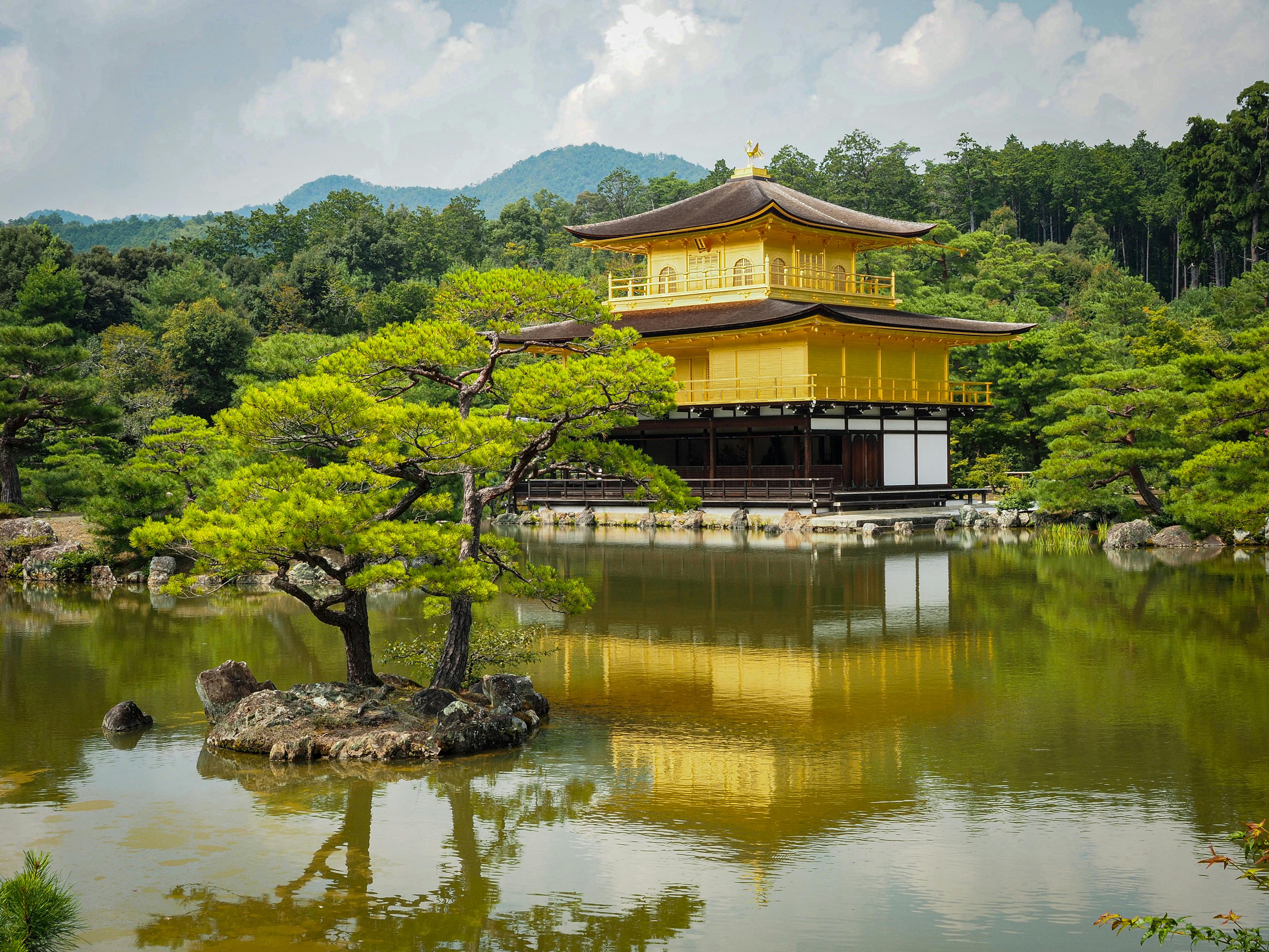 Golden temple (Kinkaku-ji) on a lake, surrounded by trees and mountains, reflecting in the water.