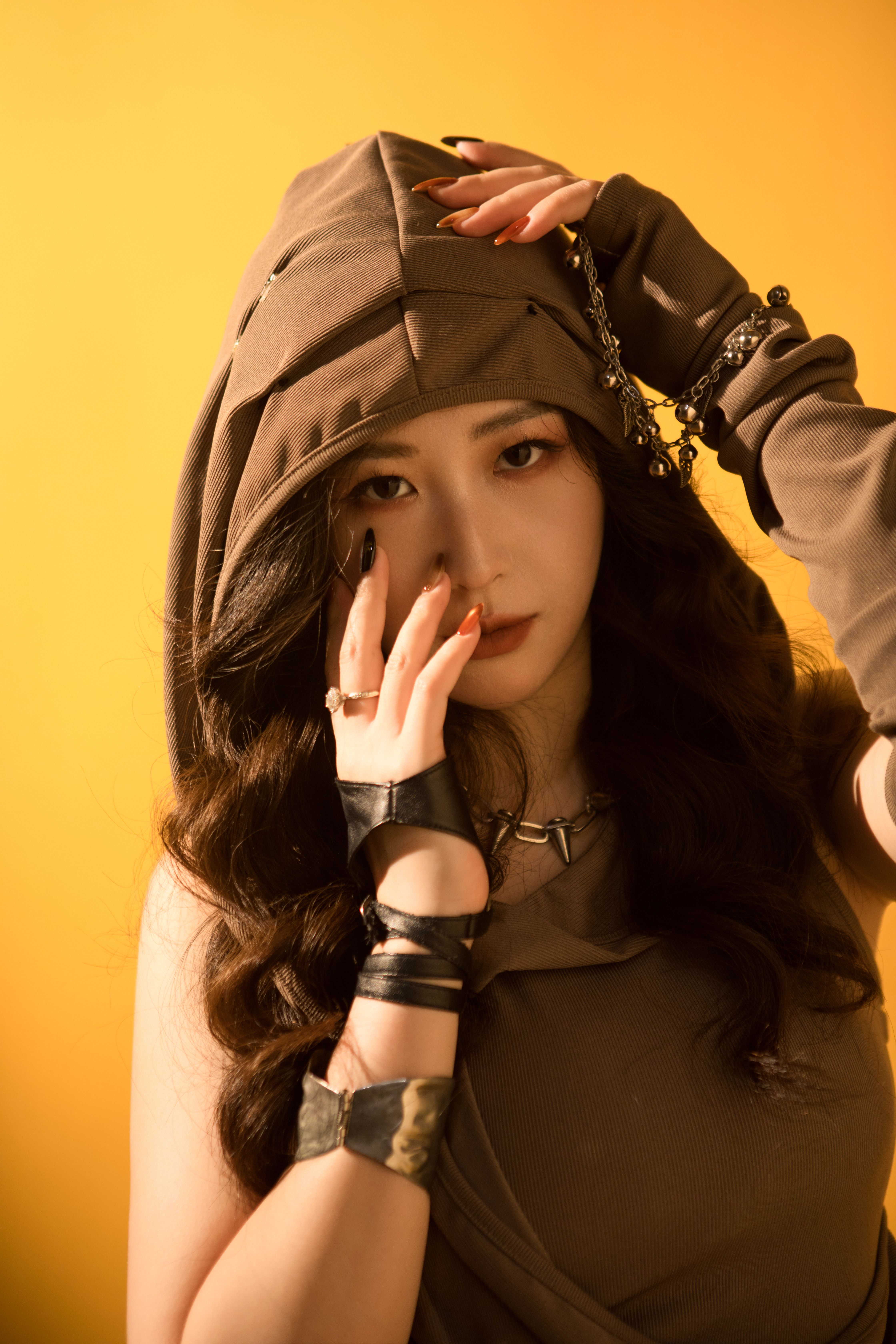 Fashionable woman in brown hoodie poses against a vibrant yellow background.