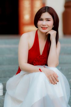 A woman in a red and white dress smiling while sitting on steps outdoors.