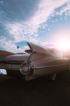 A classic pink Cadillac parked outdoors at sunrise with palm trees in the background, highlighting nostalgia and retro style.