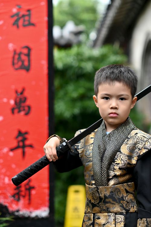 Free A young boy poses with a sword in a traditional costume against red signage. Stock Photo
