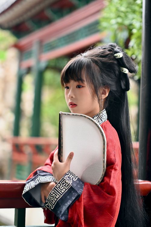 Free Portrait of a young girl wearing traditional Chinese clothing, holding a fan. Stock Photo
