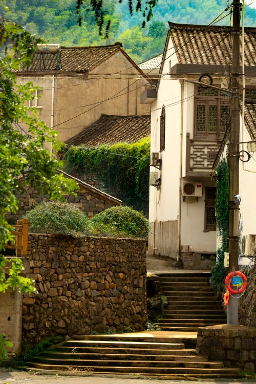 Free Quaint rustic street with stone walls and traditional architecture in a sunny village setting. Stock Photo