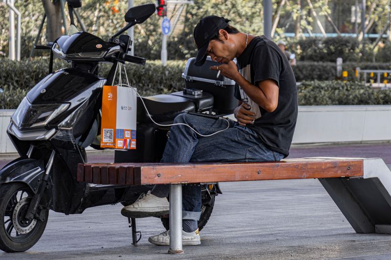 Man uses electric scooter as phone charger outdoors, capturing urban tech lifestyle.