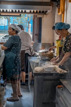 Chefs preparing food in a bustling traditional Asian kitchen setting.