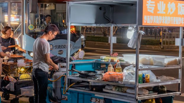 Food stall at night with two people cooking on a busy street.