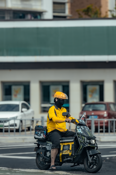 A delivery rider in yellow on an electric scooter waiting at a city intersection.