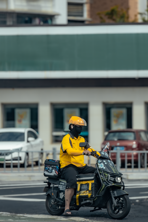 Free A delivery rider in yellow on an electric scooter waiting at a city intersection. Stock Photo