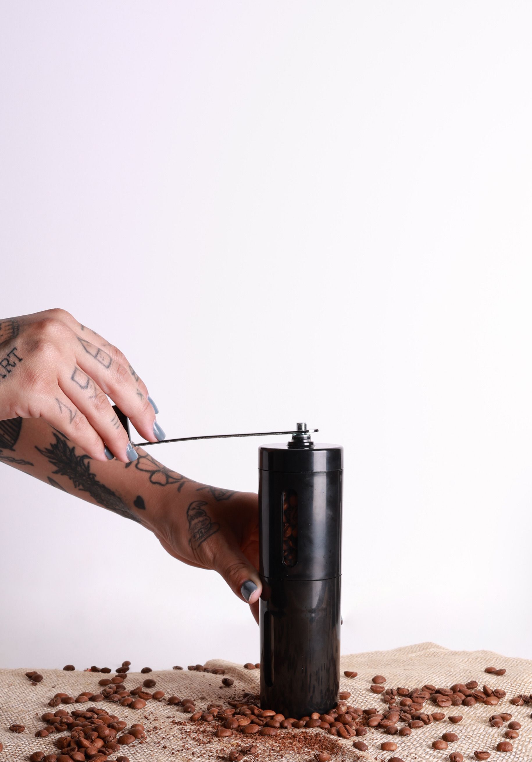Close-up of tattooed hands grinding coffee beans using a manual grinder.