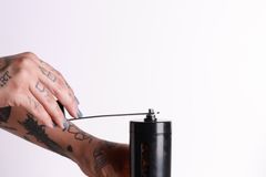Close-up of tattooed hands grinding coffee beans using a manual grinder.