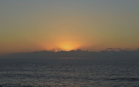 A tranquil ocean sunrise with vibrant hues of orange and yellow illuminating the sky and sea.