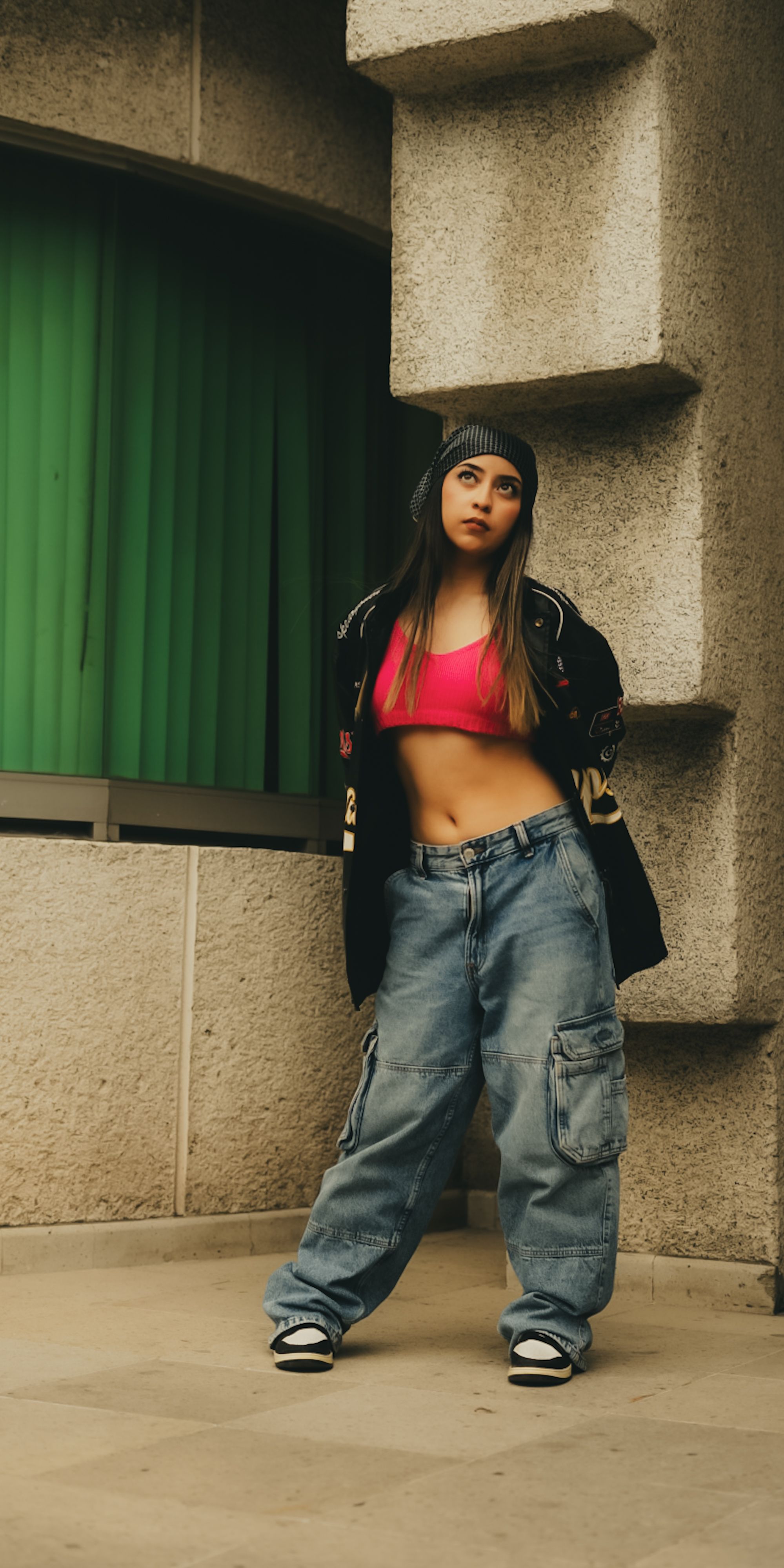 Mulher estilosa em traje de rua posando contra uma parede texturizada com uma expressão confiante.